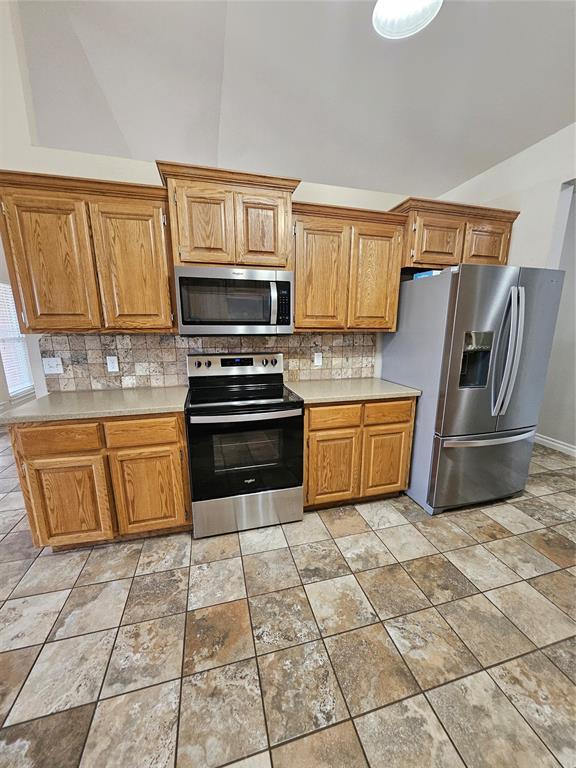1801 Caribou St, Altus, OK 73521 - kitchen with appliances with stainless steel finishes, lofted ceiling, tasteful backsplash, light countertops, and light stone finish flooring