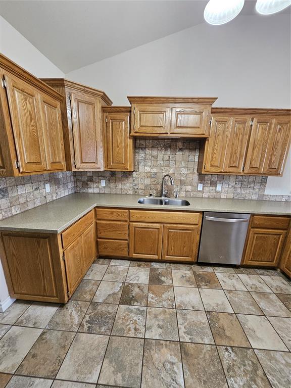 1801 Caribou St, Altus, OK 73521 - kitchen featuring a sink, dishwasher, vaulted ceiling, backsplash, and brown cabinets