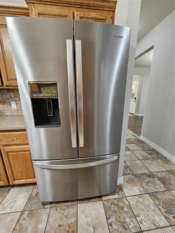 1801 Caribou St, Altus, OK 73521 - kitchen view of stainless steel refrigerator with ice dispenser, baseboards, light countertops, backsplash, and brown cabinetry