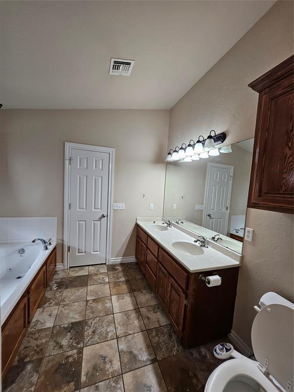 1801 Caribou St, Altus, OK 73521 - bathroom with a jetted tub, baseboards, double vanity, toilet, and vaulted ceiling