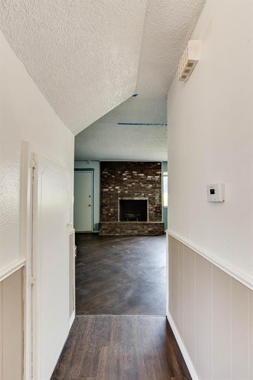 unfurnished living room with a textured ceiling, a fireplace, wood finished floors, a decorative wall, and a wainscoted wall