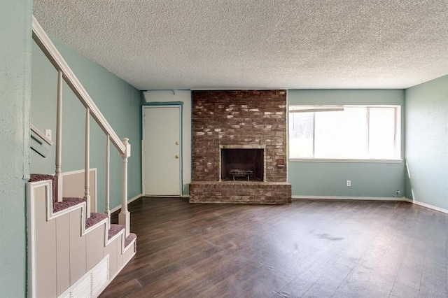 unfurnished living room featuring dark wood-style flooring, stairway, a textured ceiling, and a brick fireplace
