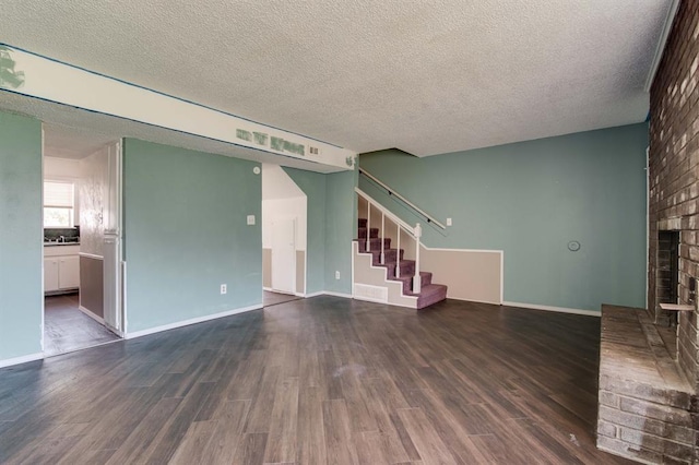 unfurnished living room featuring dark wood-type flooring, a fireplace, a textured ceiling, stairs, and baseboards