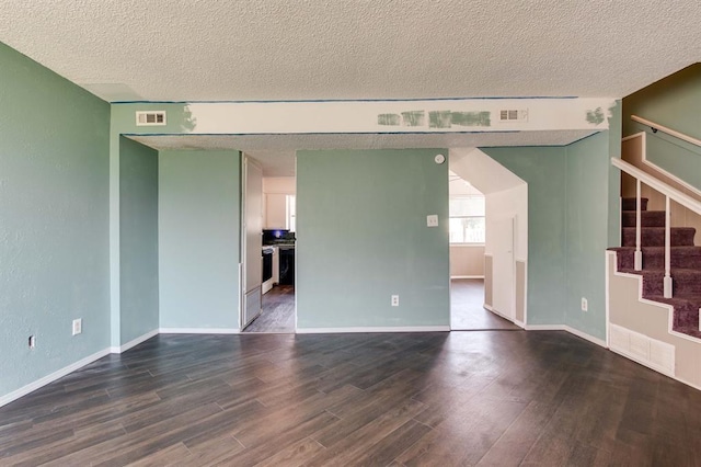 unfurnished living room featuring dark wood-style floors, a textured ceiling, stairway, and baseboards