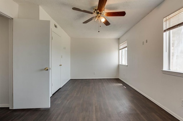 unfurnished room featuring healthy amount of natural light, dark wood-type flooring, ceiling fan, and a textured ceiling