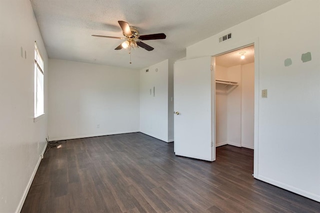unfurnished bedroom featuring dark wood-style floors, baseboards, ceiling fan, and a spacious closet