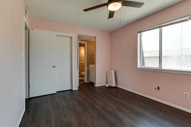 unfurnished bedroom featuring dark wood finished floors, baseboards, a textured ceiling, ensuite bathroom, and a closet