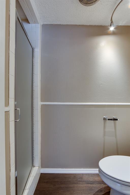 full bathroom with a shower stall, wood finished floors, toilet, a textured ceiling, and baseboards