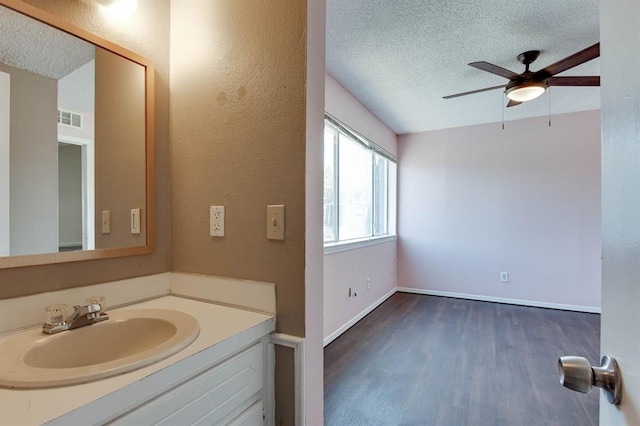 bathroom with a textured ceiling, wood finished floors, a ceiling fan, vanity, and baseboards