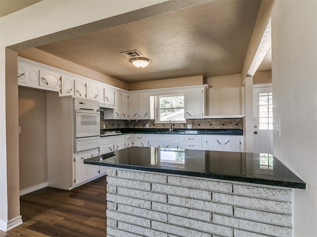 kitchen with oven, white cabinets, a sink, tasteful backsplash, and a textured ceiling