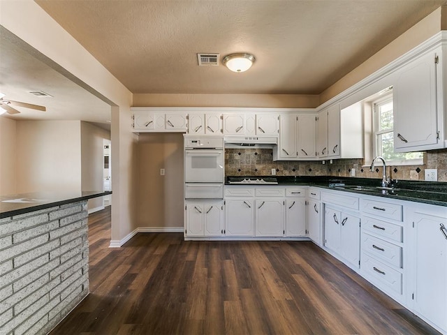 kitchen featuring oven, a sink, a warming drawer, dark countertops, and cooktop