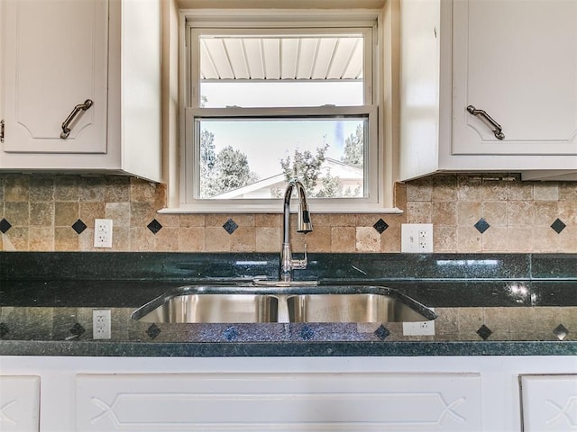 kitchen with a sink, white cabinetry, backsplash, and dark stone countertops