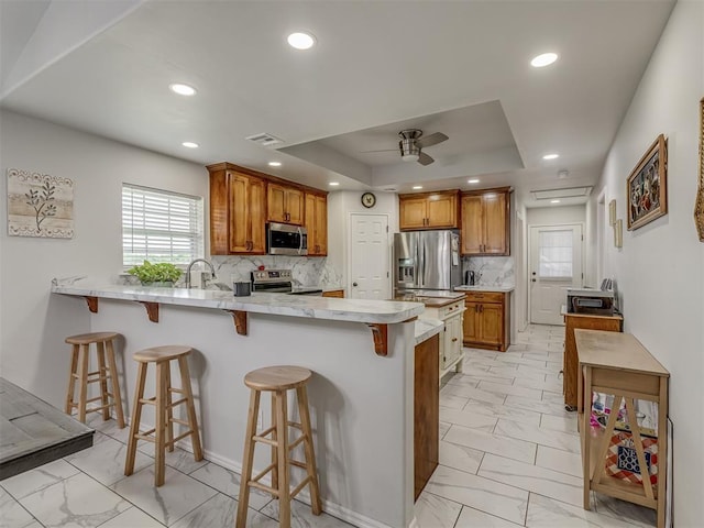 1466 County Rd 1188, Tuttle, OK 73089 - kitchen with appliances with stainless steel finishes, light marble finish floors, a ceiling fan, a peninsula, and brown cabinets
