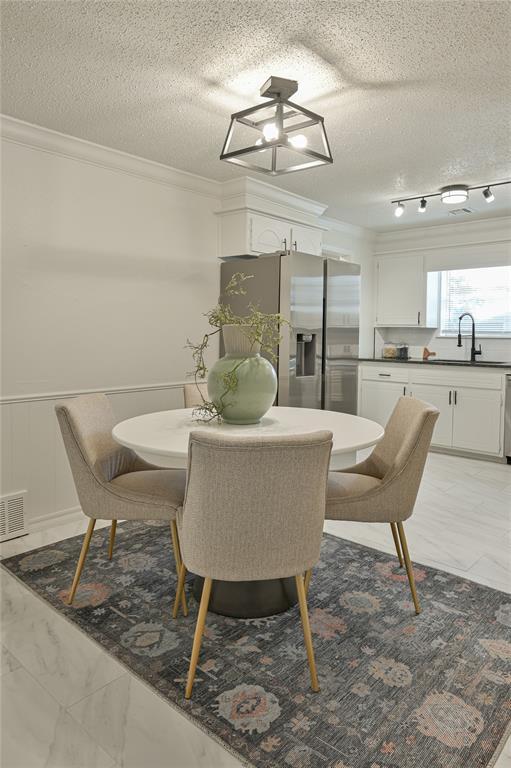 121 NW 79th St, Oklahoma City, OK 73114 - dining space featuring ornamental molding, light marble finish flooring, a textured ceiling, and wainscoting