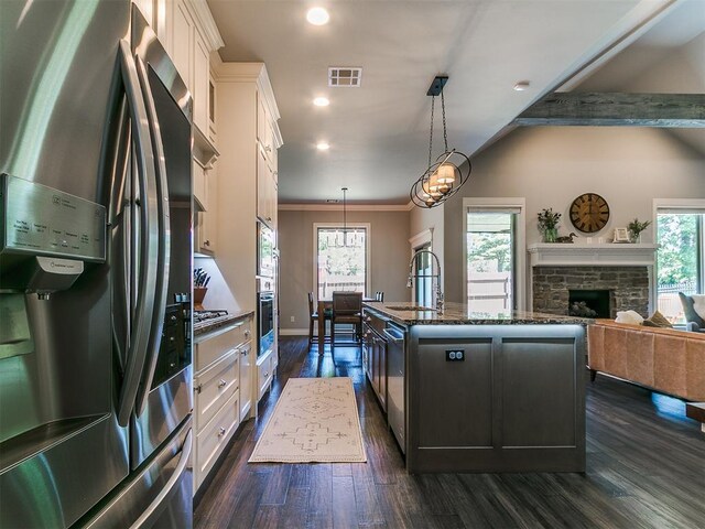 4133 Carmina Dr, Edmond, OK 73034 - kitchen featuring appliances with stainless steel finishes, a sink, a kitchen island with sink, dark wood finished floors, and dark stone counters