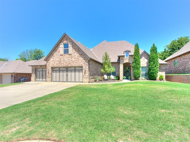 4133 Carmina Dr, Edmond, OK 73034 - french country home with concrete driveway, brick siding, a front lawn, and a shingled roof