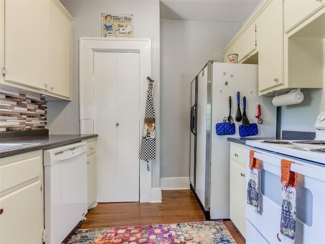 kitchen featuring white appliances, dark wood-style floors, dark countertops, decorative backsplash, and cream cabinets