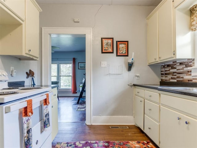 kitchen with white range with electric cooktop, dark countertops, dark wood-style flooring, decorative backsplash, and baseboards