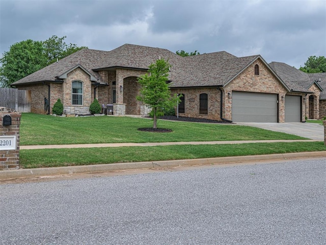 2145 Sycamore Creek Ave, Yukon, OK 73099 - french country style house with an attached garage, concrete driveway, brick siding, and a shingled roof