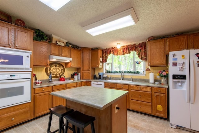 13351 El Zorro, Edmond, OK 73034 - kitchen with white appliances, a textured ceiling, under cabinet range hood, and brown cabinetry