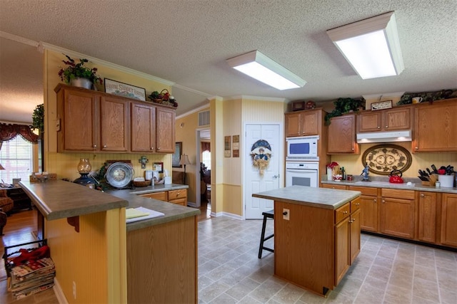 13351 El Zorro, Edmond, OK 73034 - kitchen featuring white appliances, crown molding, a breakfast bar area, a textured ceiling, and a peninsula