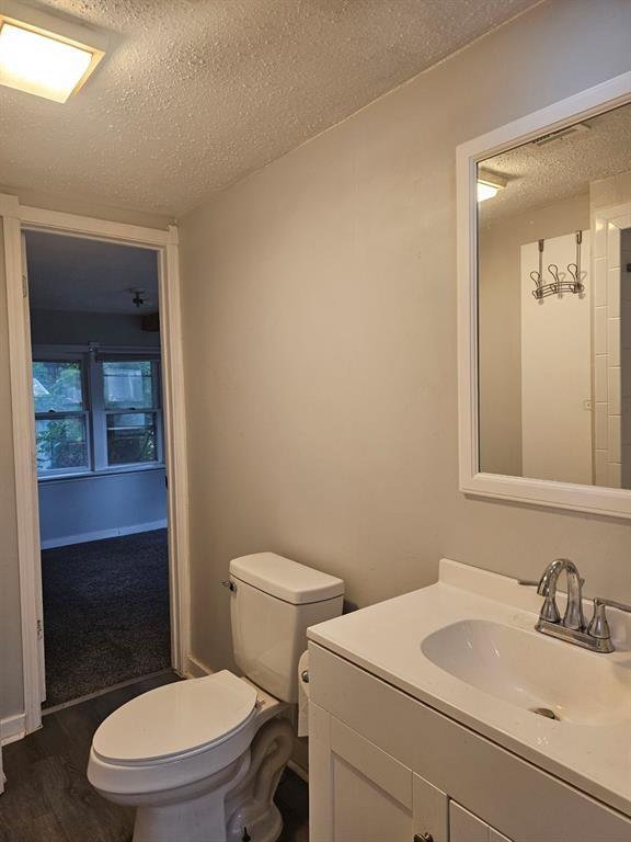 1015 W 10th Ave, Stillwater, OK 74074 - bathroom with a textured ceiling, toilet, wood finished floors, and vanity
