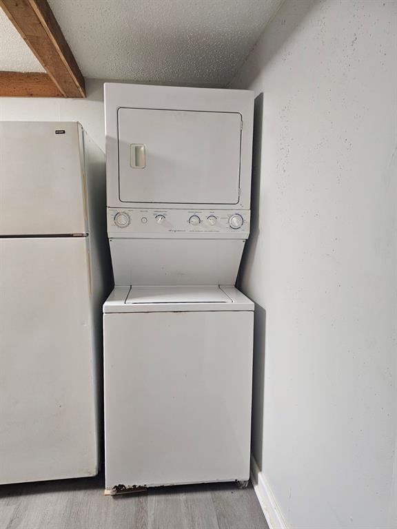 1015 W 10th Ave, Stillwater, OK 74074 - clothes washing area featuring stacked washer and clothes dryer, wood finished floors, and a textured ceiling