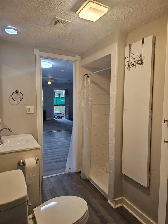 1015 W 10th Ave, Stillwater, OK 74074 - full bath featuring a sink, wood finished floors, toilet, a textured ceiling, and a shower stall