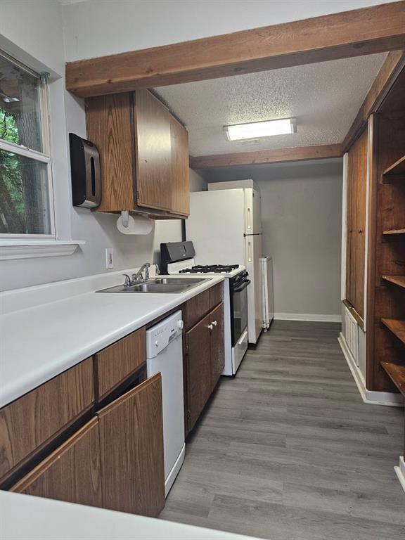 1015 W 10th Ave, Stillwater, OK 74074 - kitchen with white dishwasher, gas range oven, a sink, light countertops, and wood finished floors