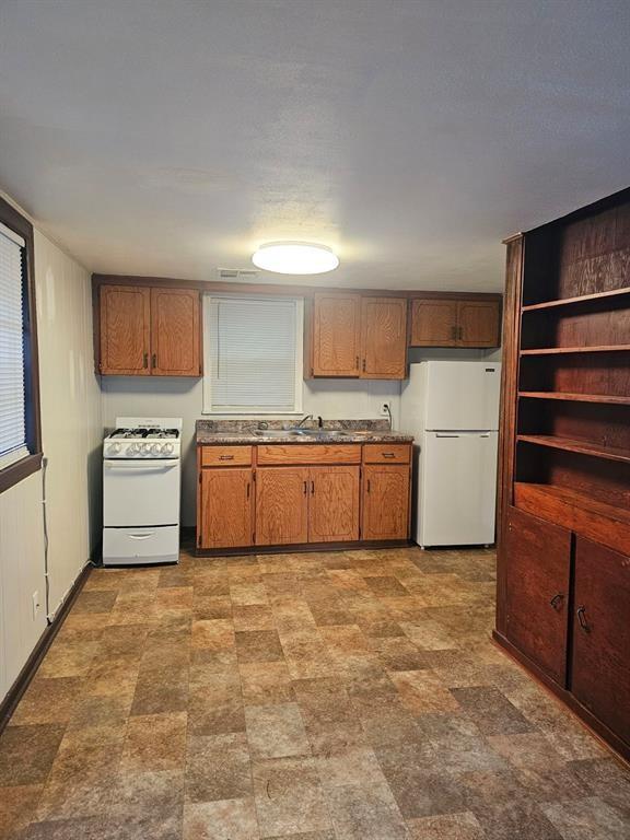 1015 W 10th Ave, Stillwater, OK 74074 - kitchen featuring white appliances, a sink, brown cabinets, and dark countertops