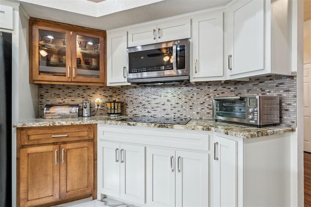 1721 Park View Pl, Edmond, OK 73003 - kitchen featuring stainless steel microwave, light stone countertops, black electric cooktop, and glass insert cabinets