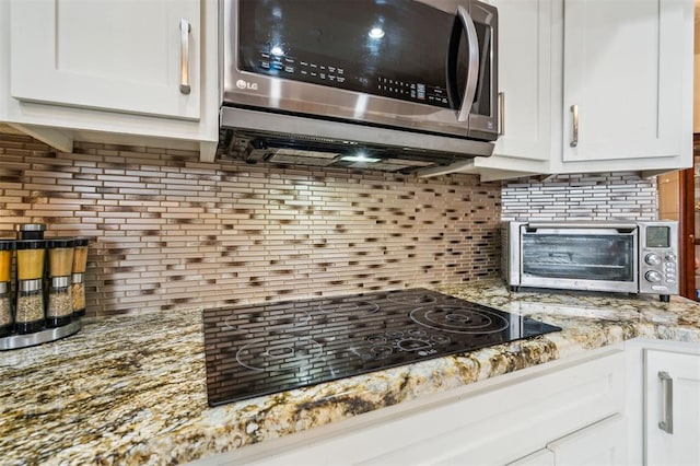 1721 Park View Pl, Edmond, OK 73003 - kitchen featuring stainless steel microwave, tasteful backsplash, white cabinets, and light stone counters
