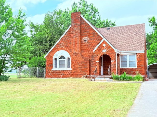 1710 W Chickasha Ave, Chickasha, OK 73018 - tudor-style house with a chimney, a shingled roof, brick siding, and a carport
