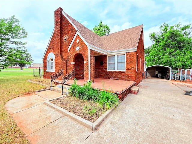 1710 W Chickasha Ave, Chickasha, OK 73018 - tudor home with a detached carport, a front yard, brick siding, roof with shingles, and concrete driveway
