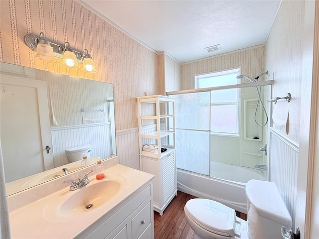 1710 W Chickasha Ave, Chickasha, OK 73018 - bathroom featuring wallpapered walls, wood finished floors, toilet, a wainscoted wall, and shower / bath combination with glass door
