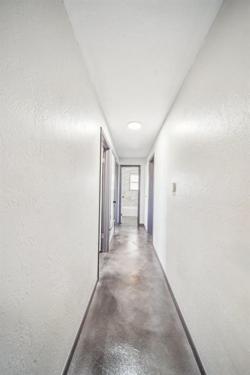 hallway with concrete flooring, baseboards, and a textured wall