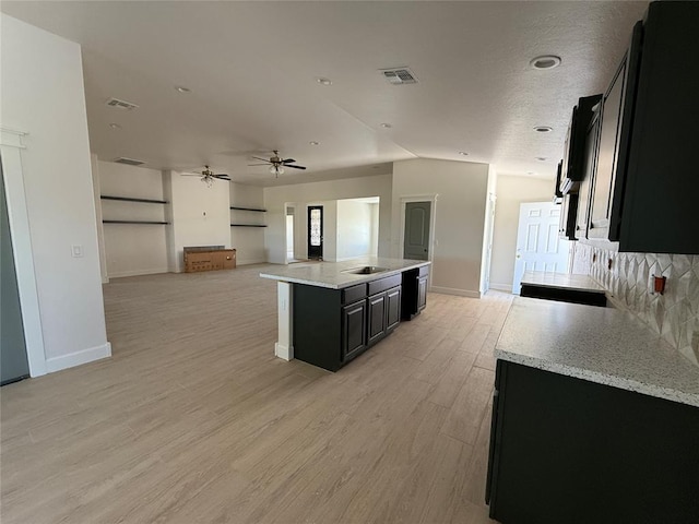 5 Old Glory Ave, Altus, OK 73521 - kitchen with dark cabinets, open floor plan, light wood finished floors, an island with sink, and decorative backsplash