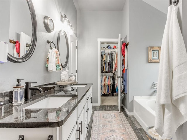 419 NE 23rd Ter, Newcastle, OK 73065 - bathroom featuring a walk in closet, vanity, baseboards, a tub, and wood finished floors