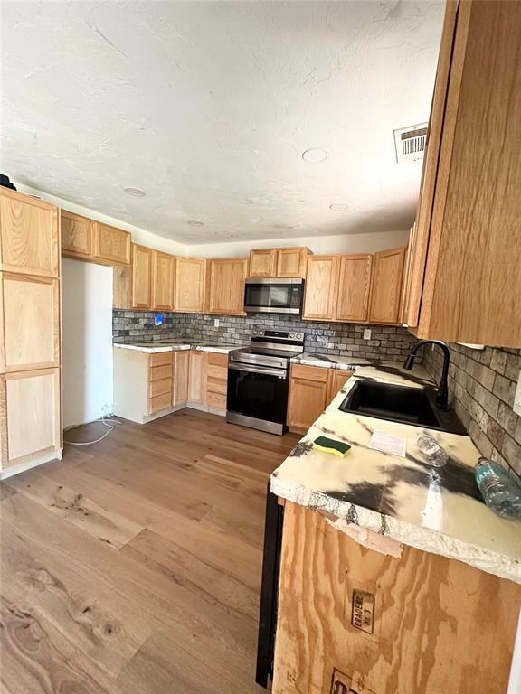 1024 Zinn Ave, Blair, OK 73526 - kitchen featuring stainless steel appliances, a sink, light wood-style flooring, decorative backsplash, and light countertops