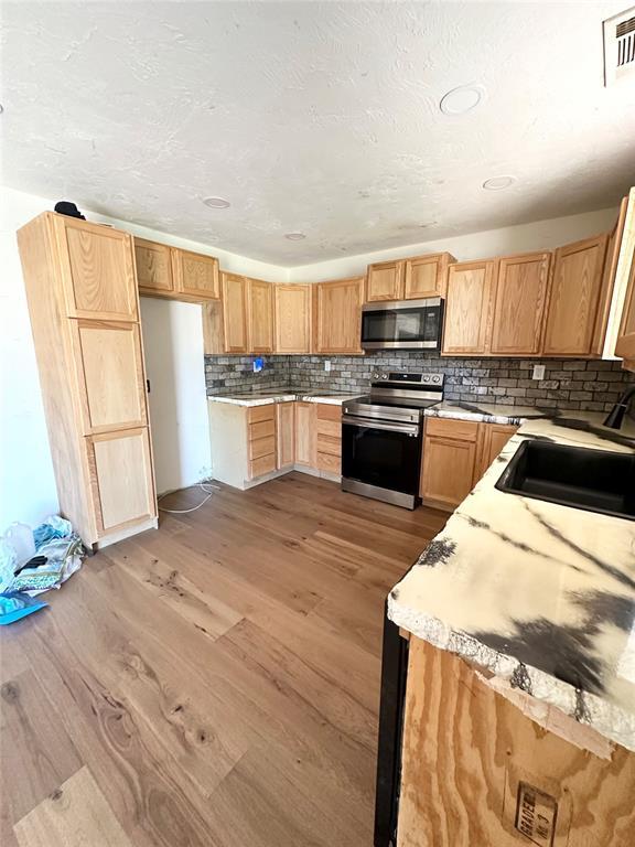1024 Zinn Ave, Blair, OK 73526 - kitchen featuring appliances with stainless steel finishes, a sink, light wood finished floors, backsplash, and light countertops