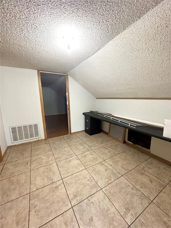 1024 Zinn Ave, Blair, OK 73526 - additional living space with a textured ceiling, vaulted ceiling, light tile patterned flooring, and baseboards