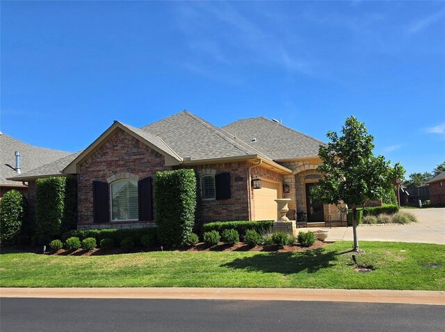 5608 NW 127th St, Oklahoma City, OK 73142 - french country home featuring an attached garage, a front yard, a shingled roof, and brick siding