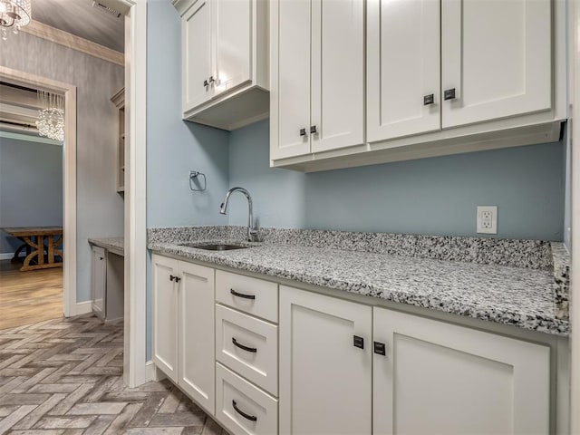 832 Gateway Bridge Rd, Edmond, OK 73034 - kitchen with a sink, light stone counters, white cabinets, baseboards, and a chandelier