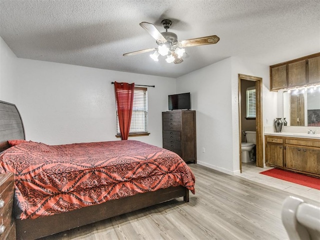 bedroom featuring light wood-style flooring, a textured ceiling, connected bathroom, a ceiling fan, and baseboards