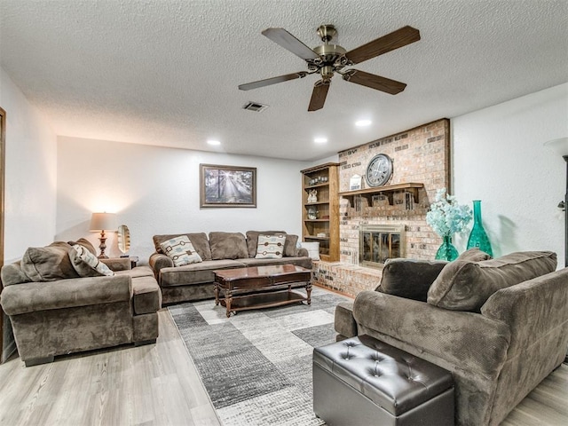 living room featuring a ceiling fan, a textured ceiling, a brick fireplace, light wood-style floors, and recessed lighting