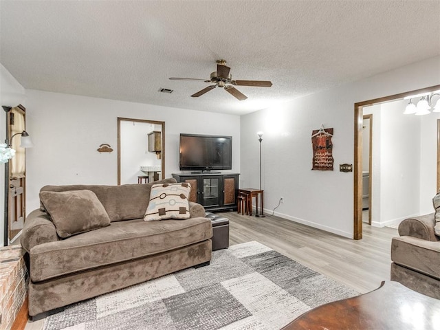 living room featuring light wood-type flooring, a ceiling fan, a textured ceiling, and baseboards