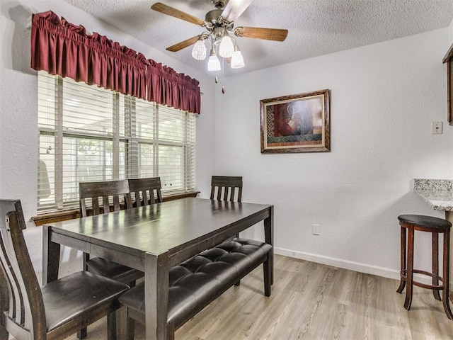 dining area featuring light wood-style floors, a ceiling fan, a textured ceiling, and baseboards