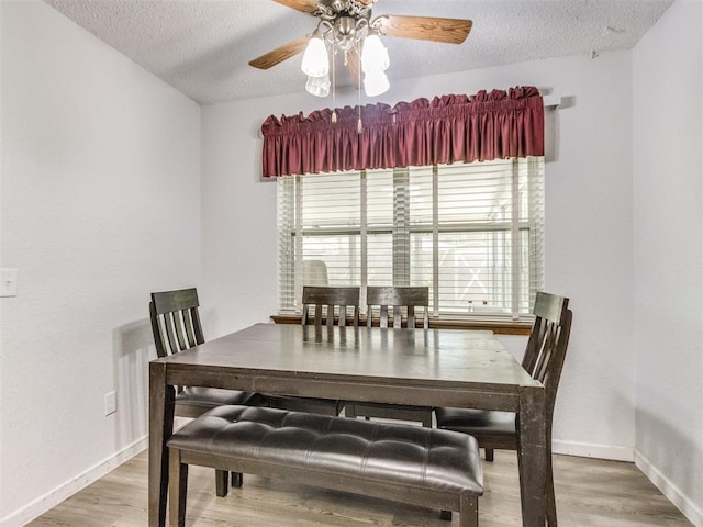dining room with light wood finished floors, a textured ceiling, baseboards, and a ceiling fan