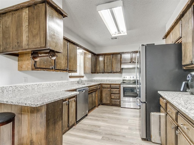 kitchen featuring appliances with stainless steel finishes, a sink, a textured ceiling, light wood-style flooring, and light stone countertops