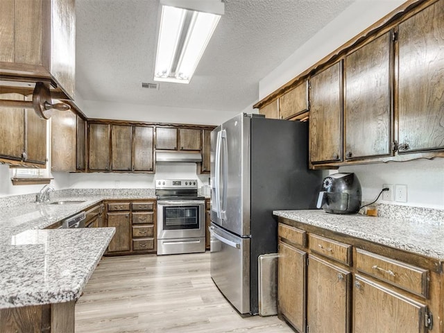 kitchen with stainless steel appliances, a sink, under cabinet range hood, a textured ceiling, and light wood finished floors